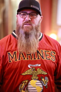 A man with long beard and glasses wearing a red shirt.