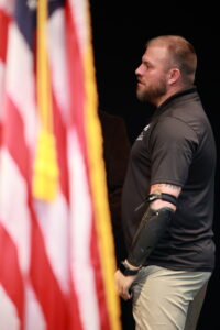 A man with a tattoo on his arm stands in front of an american flag.