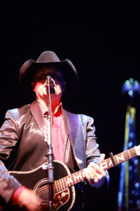 A man in a cowboy hat and suit playing guitar.