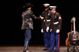 A man in black jacket shaking hands with two men in military uniforms.