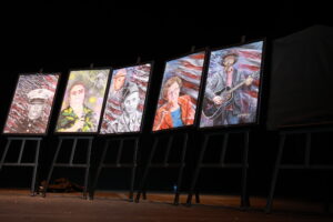 A row of easels with paintings on them.