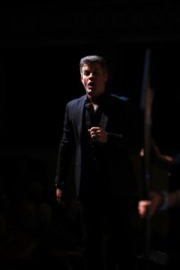 A man in black jacket holding a microphone.